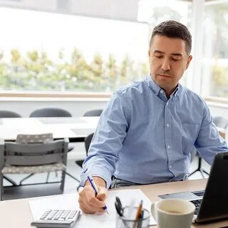 Man writing at desk with laptop and coffee