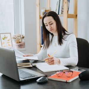 Woman writing at home office desk with laptop